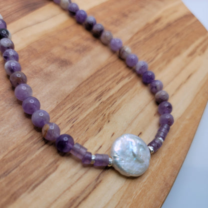 Amethyst and coin pearl necklace on a wood platform on a white background