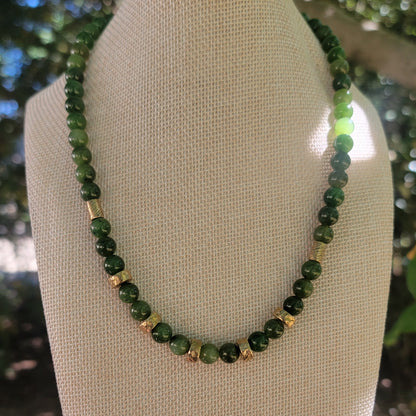 Green beaded necklace with bronze bead accents on a linen bust in an outdoor environment.