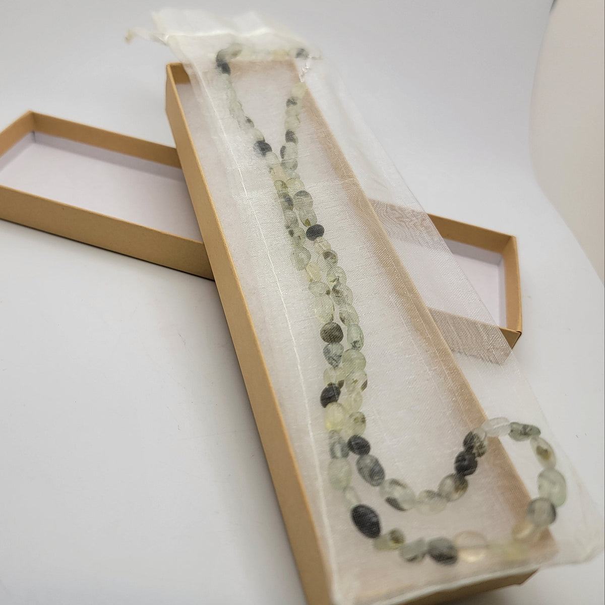 Green and black beaded necklace in organza bag in cardboard gift box on white background