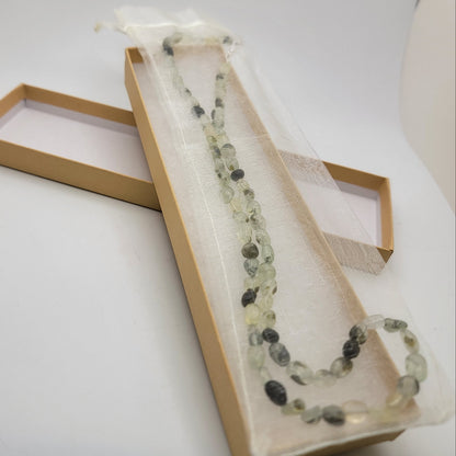 Green and black beaded necklace in organza bag in cardboard gift box on white background